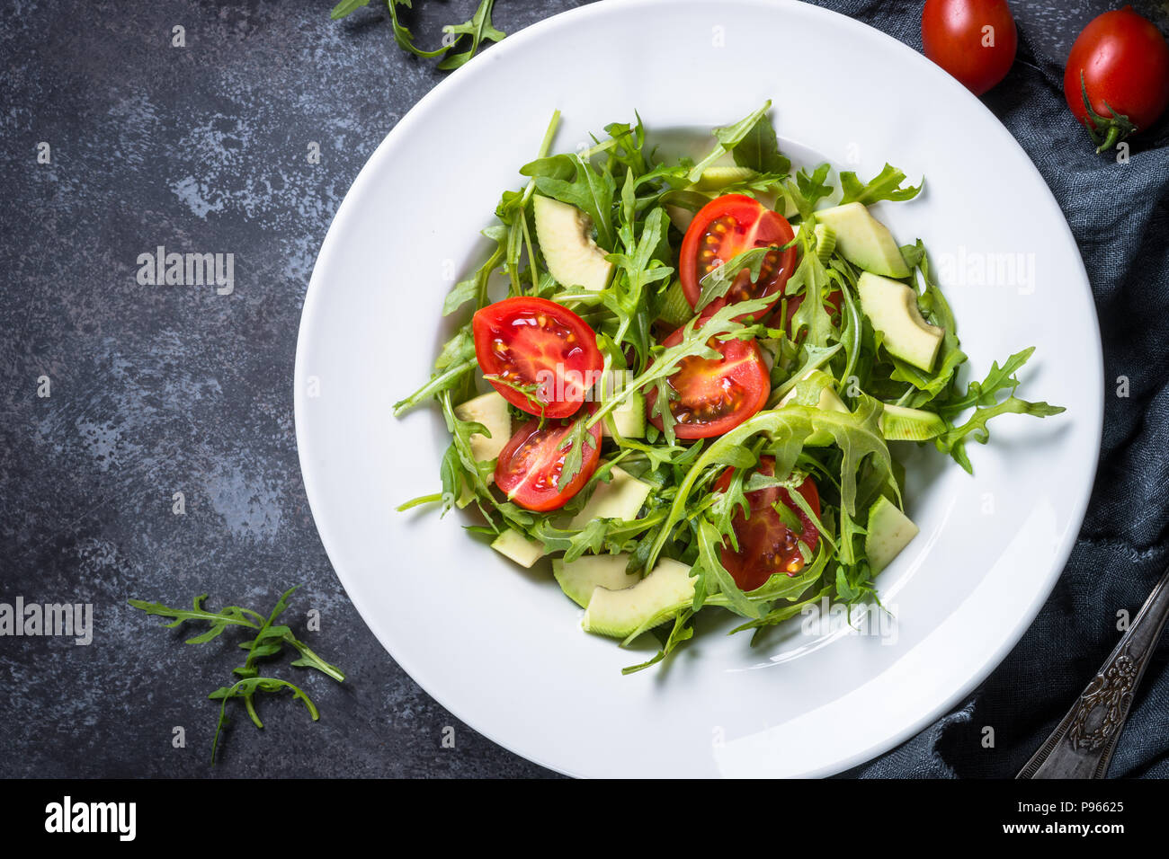 Grüner Salat aus Rucola, Avocado, Tomaten. Draufsicht auf schwarz Tisch aus Stein. Stockfoto