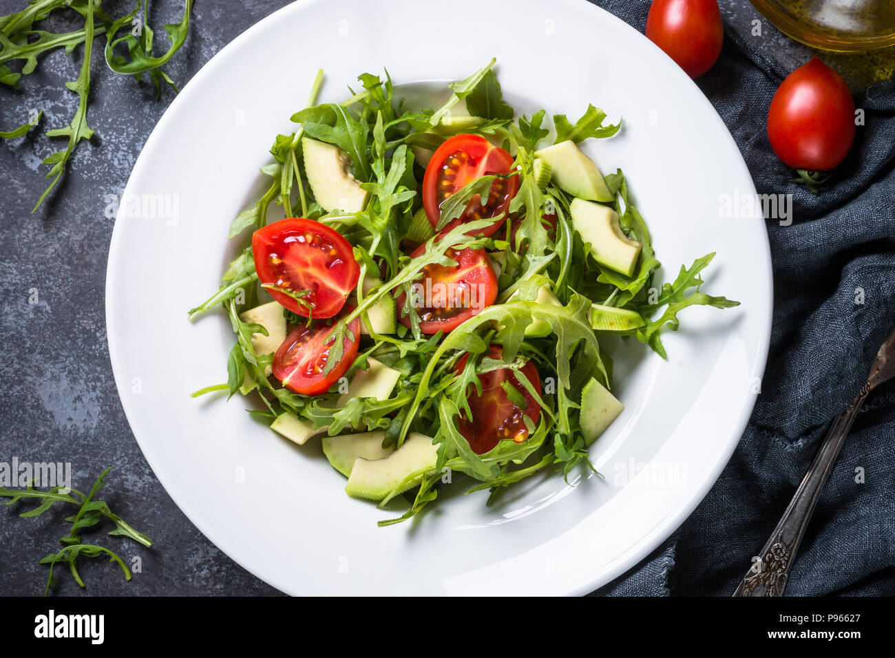 Gesund vegan Salat aus Rucola, Avocado, Tomaten. Draufsicht auf schwarz Tisch aus Stein. Stockfoto