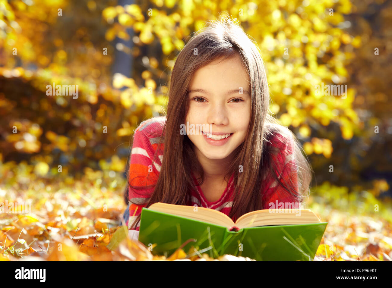 Mädchen liegt auf Laub und ein Buch lesen Stockfoto