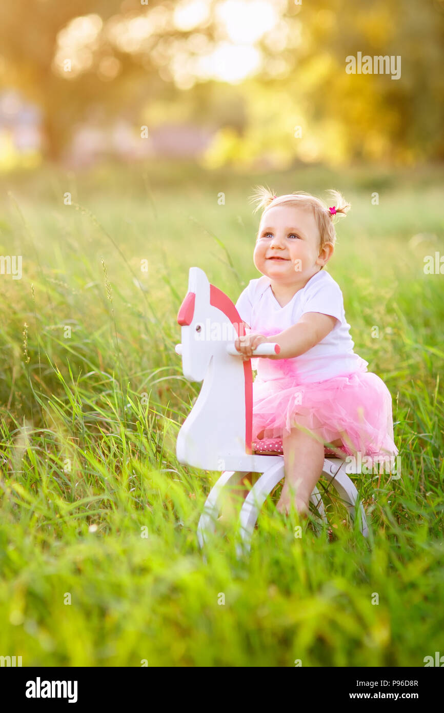 Wunderschöne kleine Mädchen in rosa Kleid reiten auf Holzspielzeug Pferd im Freien Stockfoto
