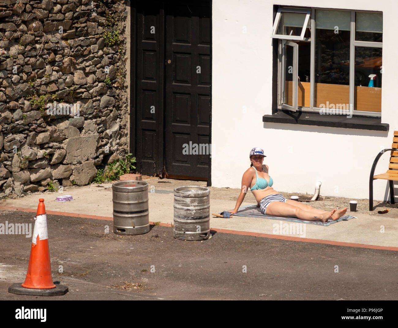 Heatwave Irland junge Frau genießt Sonnenbaden auf lustige Art und Weise auf Betonoberfläche im Hinterhof des Hauses als urban lustig ungewöhnlich Sonnenbaden. Stockfoto