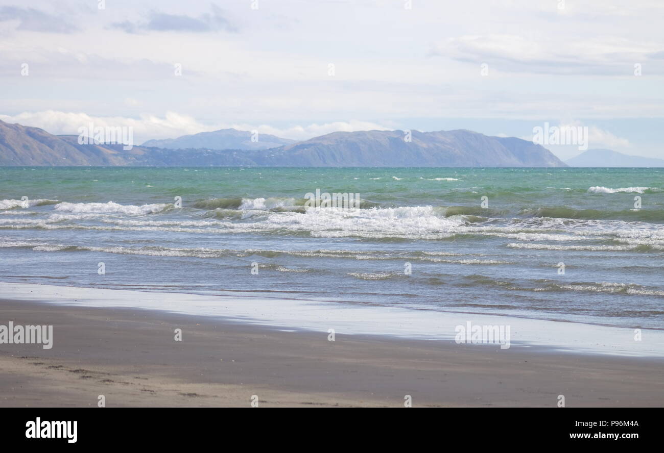 Wellen auf Raumati Strand mit Blick in Richtung Pukerua Bay und Porirua auf der unteren Westküste der Nordinsel von Neuseeland. Stockfoto