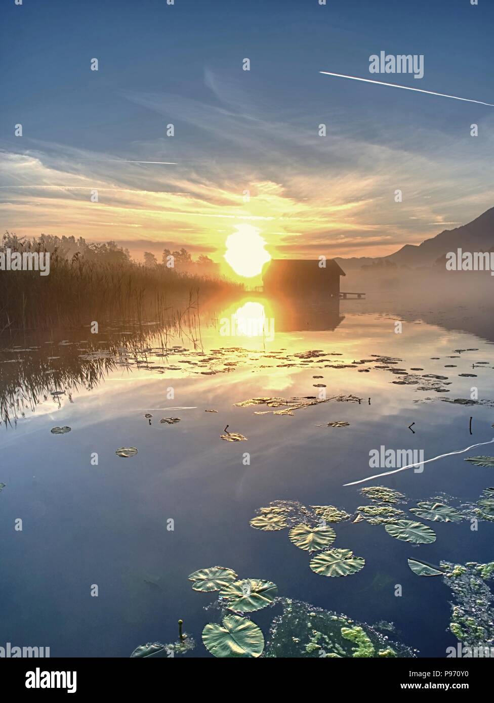 Romantischen sonnenaufgang Reflexion auf dem Kochelsee gegen Bootshäusern. Anfang Sommer morgen ansehen, Bayern, Deutschland Stockfoto