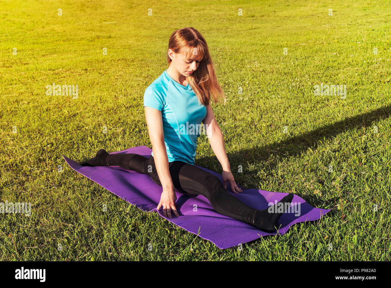 Eine dunkelhaarige Frau Trainer in einem sportlichen kurzen Top und Fitnessraum leggings macht eine breite Garn auf der Wolldecke für Yoga Hände werden nach oben gerichtet auf die Yogamatte angehoben, Hand Stockfoto