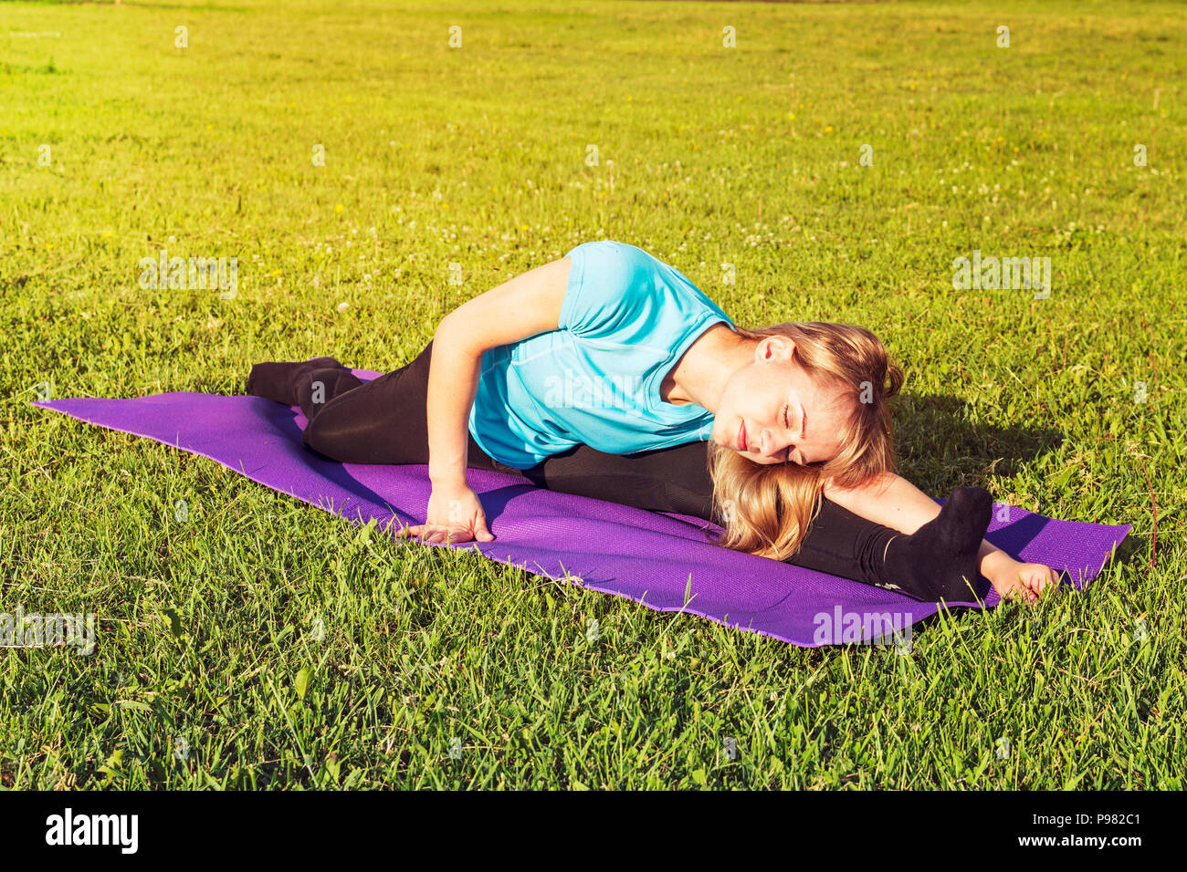 Blonde Frau Trainer in einem sportlichen kurzen Top und Fitnessraum leggings macht eine breite Garn auf der Wolldecke für Yoga Hände werden nach oben gerichtet auf die Yogamatte angehoben, im Sommer Stockfoto