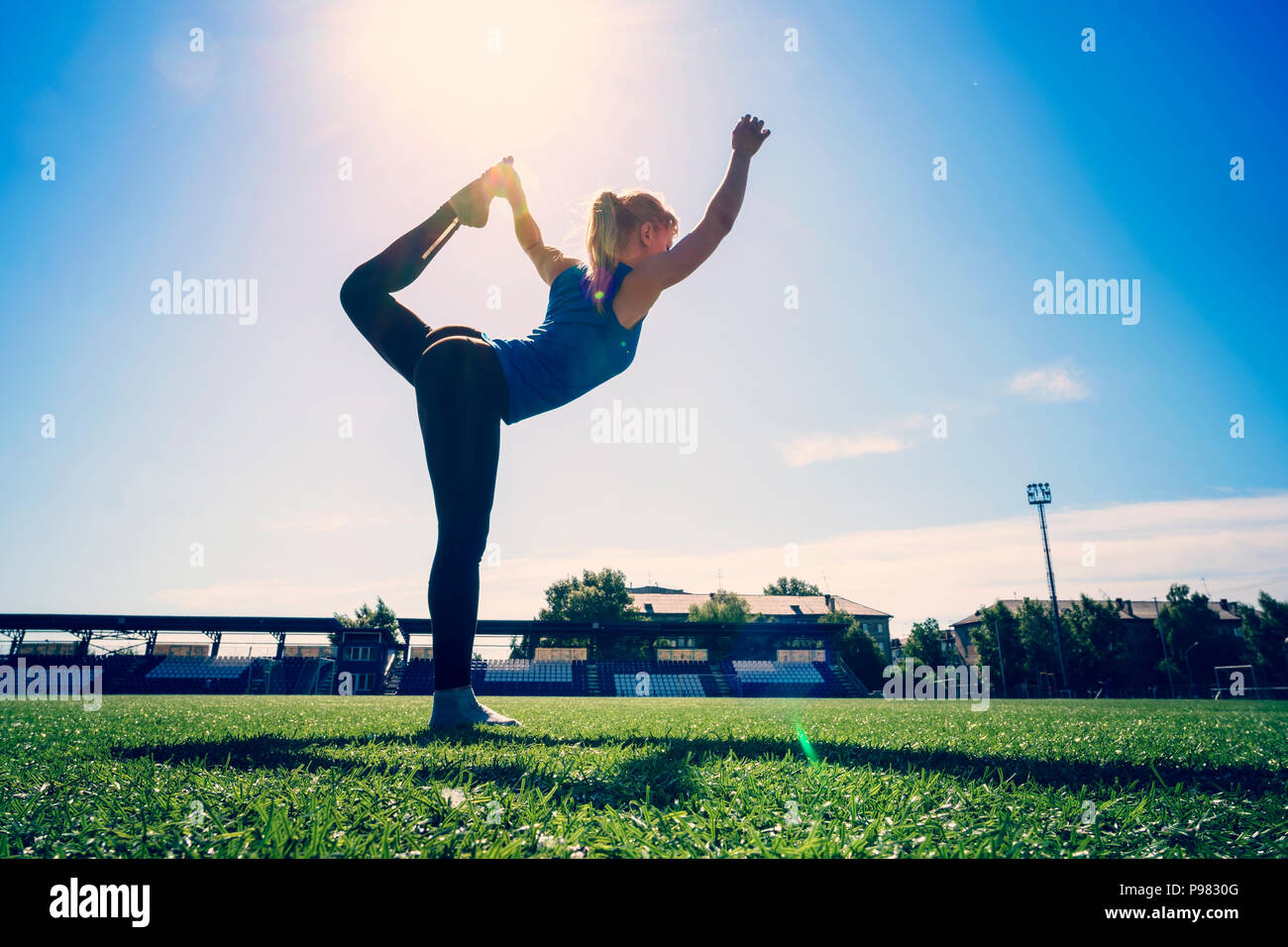 Junge Sportlerin dabei warm-up Balance übung Stehen auf einem Bein Beine dehnen und wieder im Freien. Warm-up Stretching im Stadion. Stockfoto