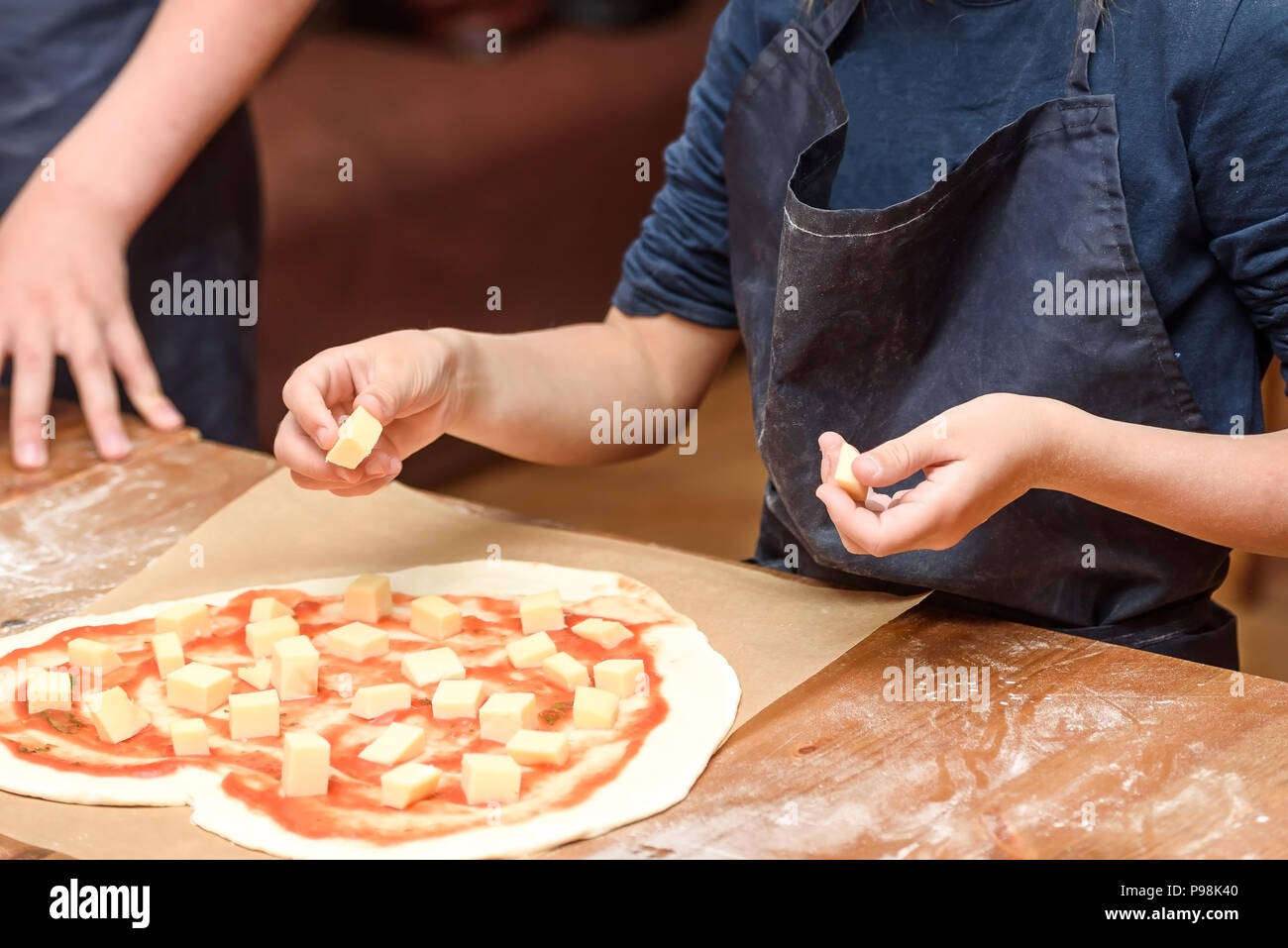 In der Nähe von Kinderhänden Vorbereitung Pizza. Kinder legen Sie auf der Grundlage der Pizza Gemüse und Käse Stockfoto