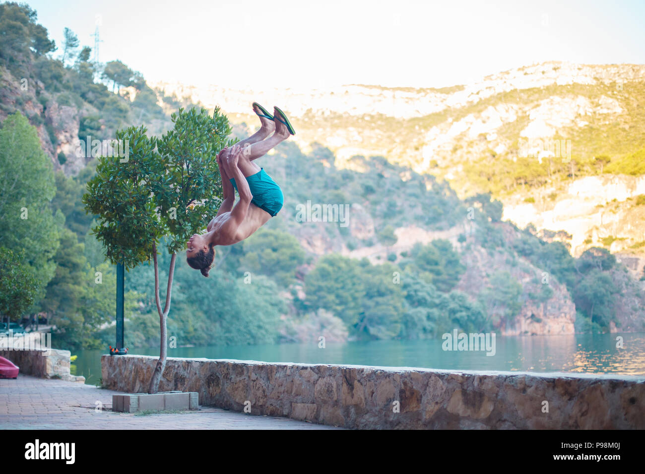 Junger Mann eine Seite blättern oder Salto beim Üben Parkour auf einem See in die Landschaft. Stockfoto