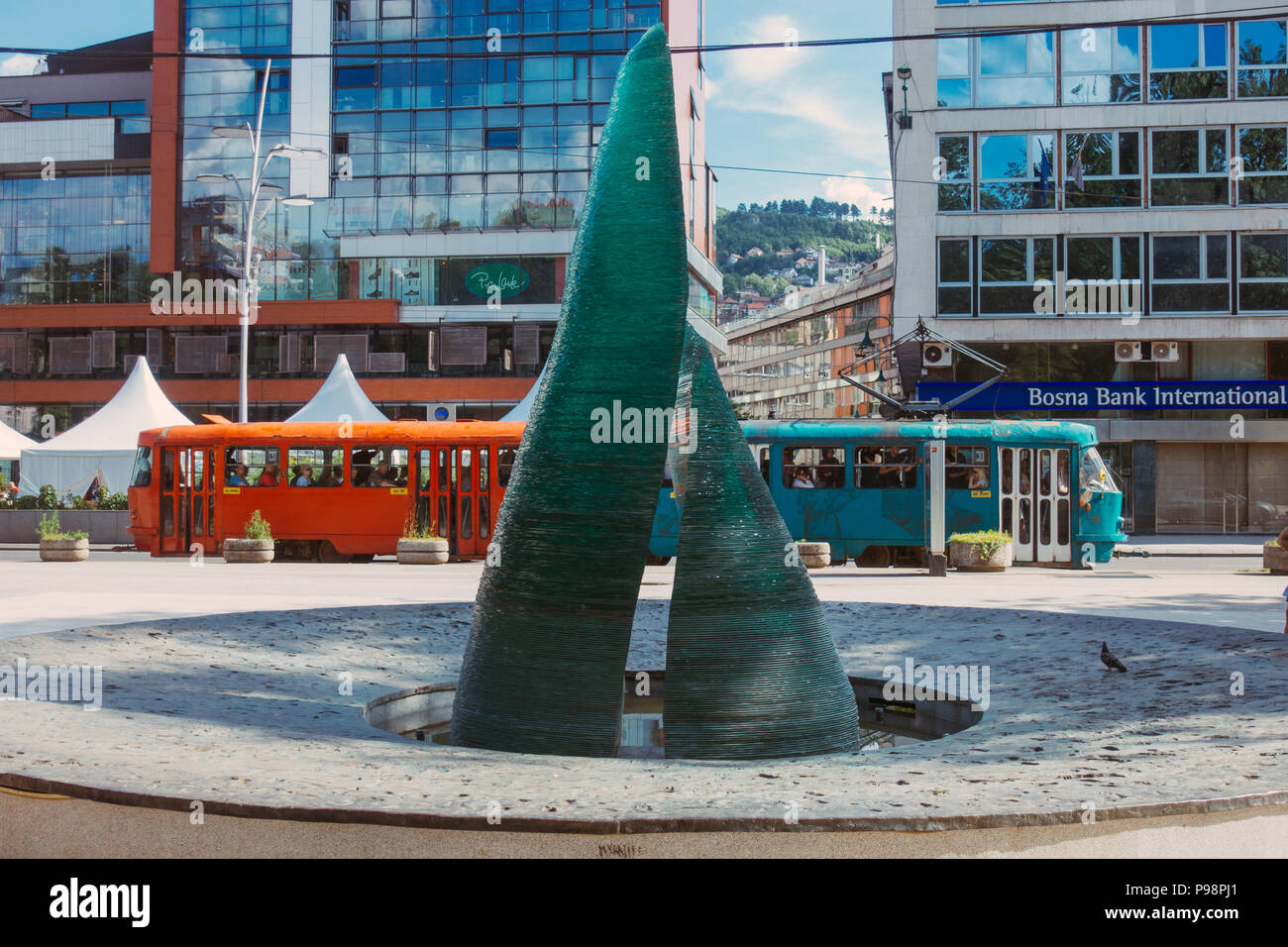 Eine Glasskulptur, die als Teil eines Gedenkens für die während der Belagerung von Sarajevo getöteten Kinder errichtet wurde. Hinter dem Hotel fährt eine Straßenbahn vorbei Stockfoto