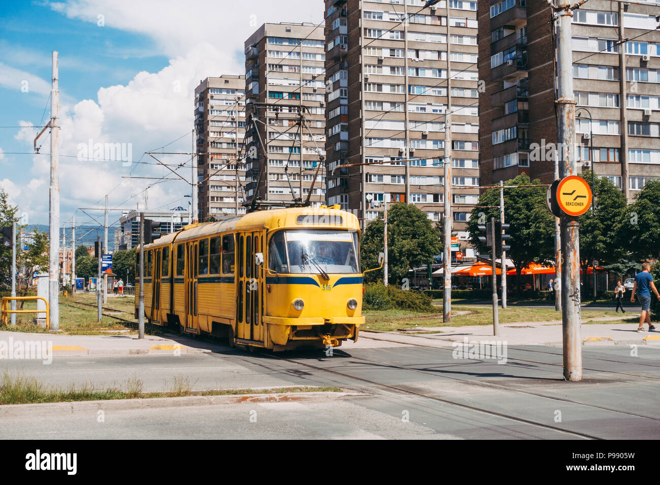 Eine gelbe Tatra T3-straßenbahnwagen überquert die Straße am Stadtrand von Sarajevo, Bosnien und Herzegowina Stockfoto