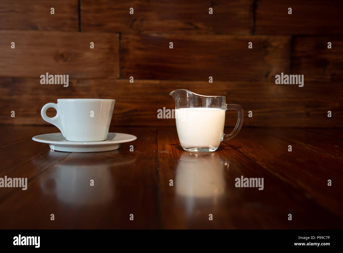 Milch in Glas Milchkännchen mit weißer Schale und Reflexion von einem Holztisch Stockfoto
