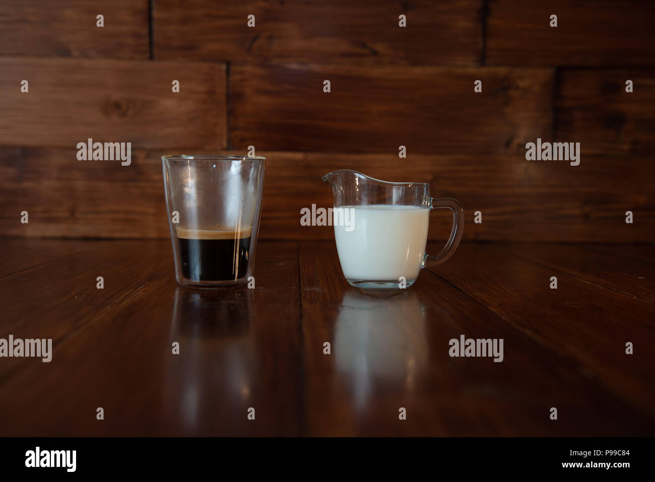 Milch in Glas Milchkännchen mit einer Tasse Kaffee in einem durchsichtigen Glas Stockfoto