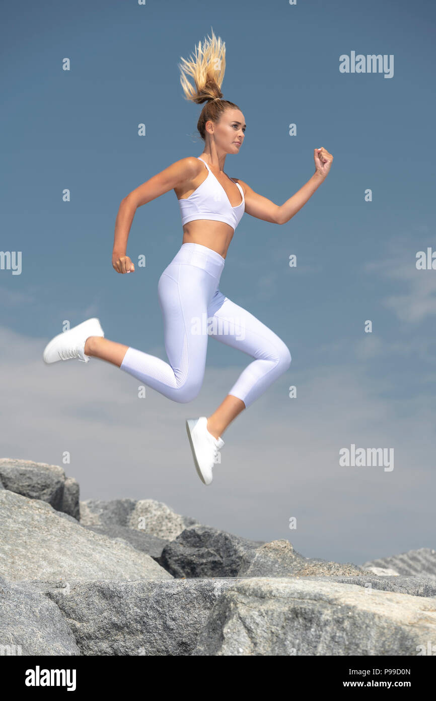 Attraktive sportliche Frau laufen und springen über Felsen, fit zu bleiben. Stockfoto