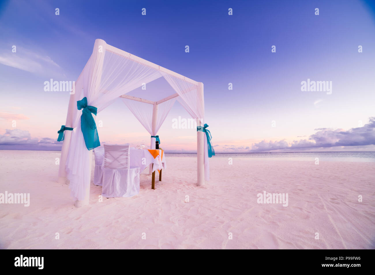 Romantisches Abendessen Tisch Set-up für eine Hochzeitsreise Paar am Strand unter Sonnenuntergang Himmel. Exotische Hochzeit und Flitterwochen Konzept Stockfoto