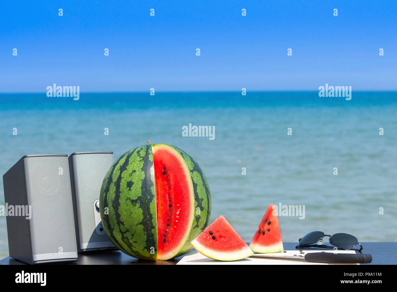 Paar Lautsprecher, ganzen und geschnittenen Wassermelone mit Messer und Schneidebrett aus Holz und eine Sonnenbrille am Strand im Sommer bereit für den Sommer. Stockfoto