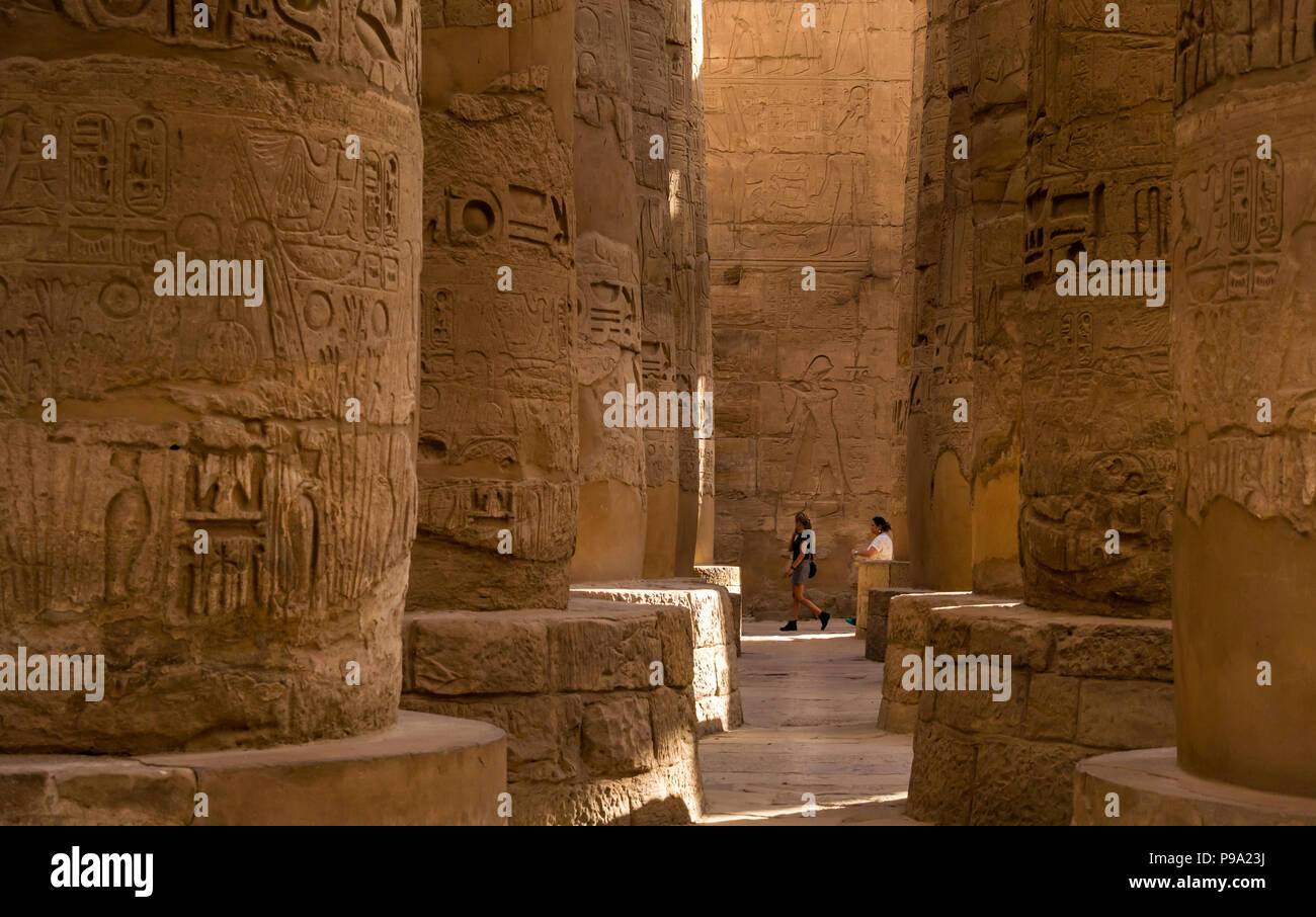 Frauen gehen zwischen den riesigen Steinsäulen mit ägyptischen Hieroglyphen in der großen Säulenhalle, Revier des Amun Ra, Karnak Tempel. Luxor, Ägypten, Afrika Stockfoto