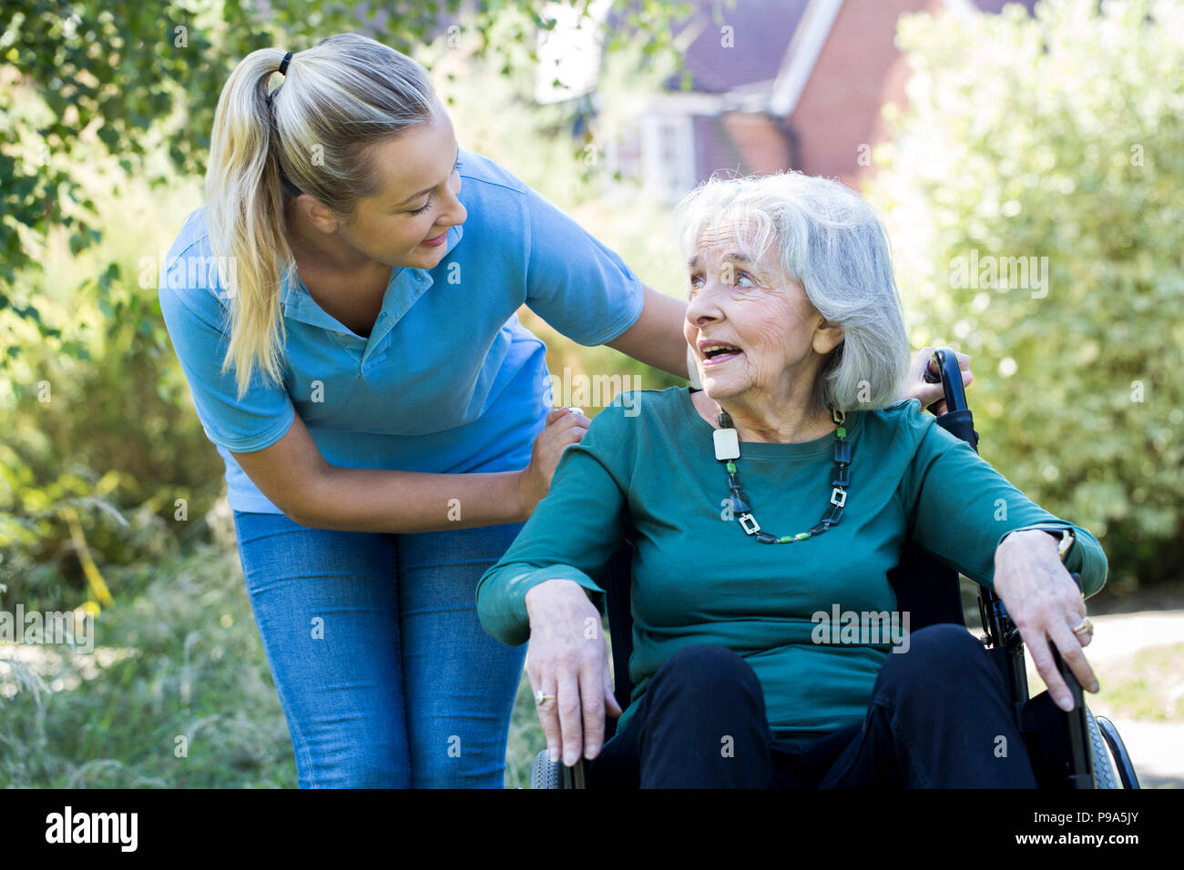 Pflegeperson Drücken ältere Frau im Rollstuhl im Garten Stockfoto