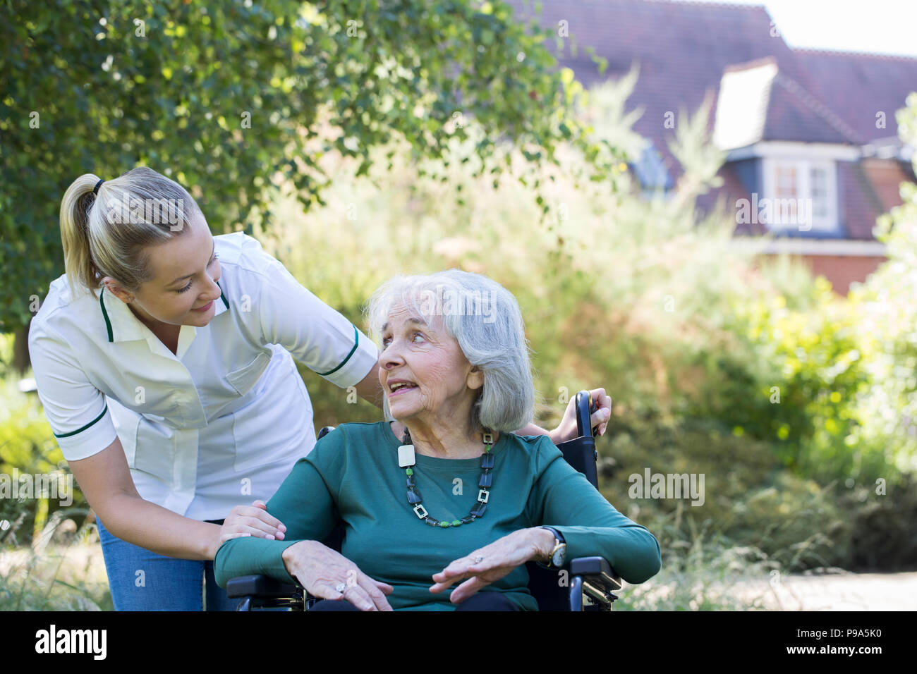 Pflegeperson Drücken ältere Frau im Rollstuhl im Garten Stockfoto