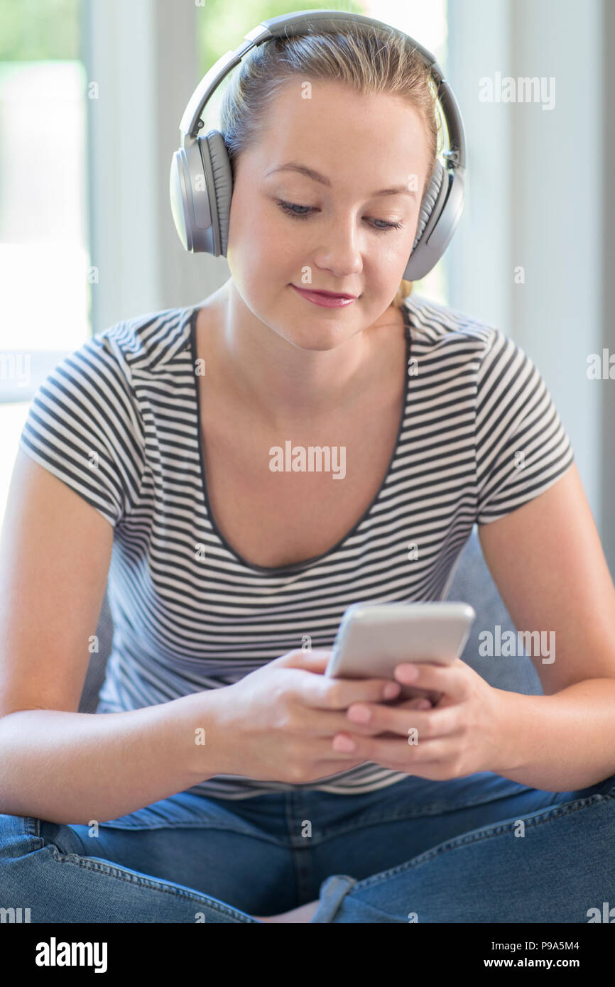 Frau zu Hause streamt Musik vom Mobiltelefon über kabellose Kopfhörer Stockfoto