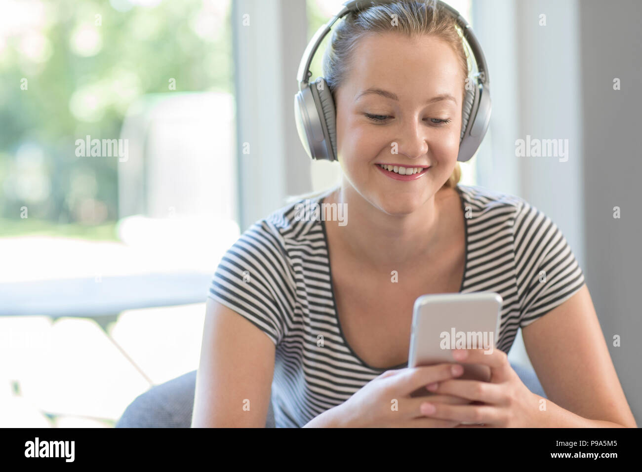Frau zu Hause streamt Musik vom Mobiltelefon über kabellose Kopfhörer Stockfoto