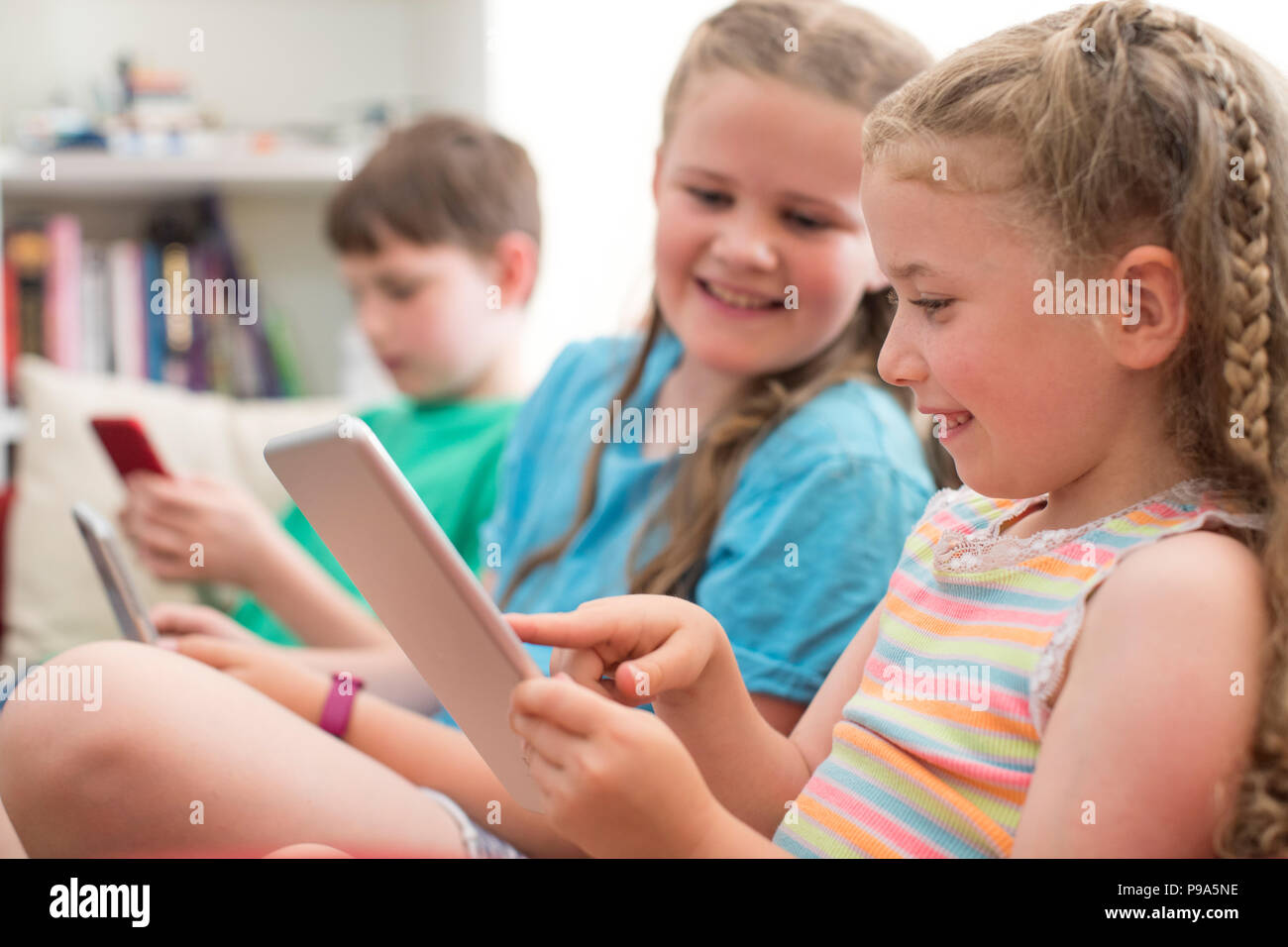 Drei Kinder auf dem Sofa zu Hause spielt mit digitalen Geräten Stockfoto