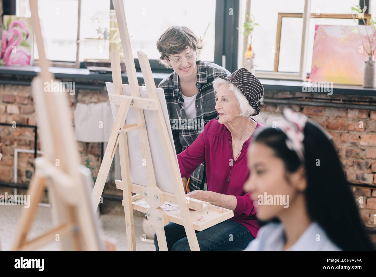 Portrait des modernen Senior Frau Malerei an der Staffelei im Atelier ein Studium der Kunst mit lächelnd weibliche Lehrer, Kommentare, Szene, in geräumigen su Sitzen Stockfoto