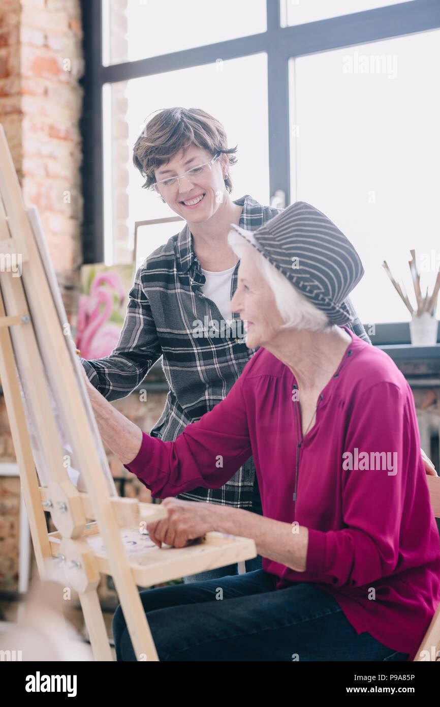 Seitenansicht Porträt des modernen Senior Frau Malerei sitzen an der Staffelei im Atelier ein Studium der Kunst mit lächelnd weibliche Lehrer, Kommentare, Szene, in s Stockfoto