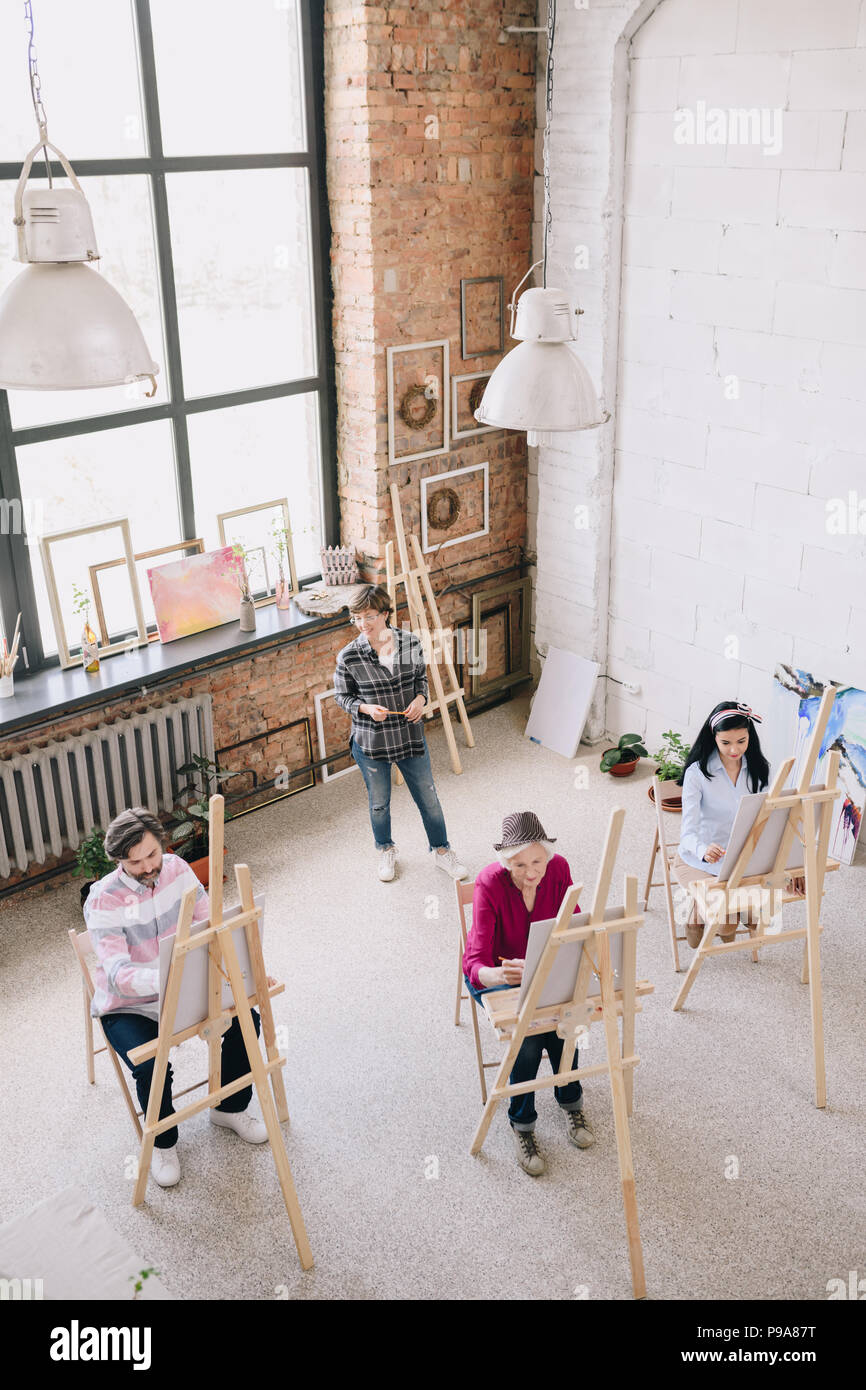 Hohe Betrachtungswinkel Porträt der weiblichen Kunst Lehrer arbeiten mit einer Gruppe von Studenten Malerei an staffeleien in geräumigen sonnigen Art Studio, Kopie Raum Stockfoto
