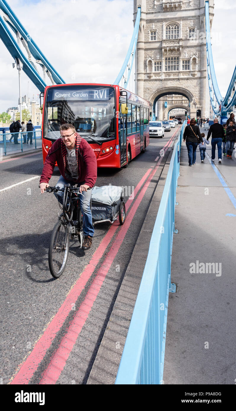 Kopf auf Hochformat eines Radfahrers über von einem roten Londoner Bus über die Tower Bridge reisen überholt werden Stockfoto