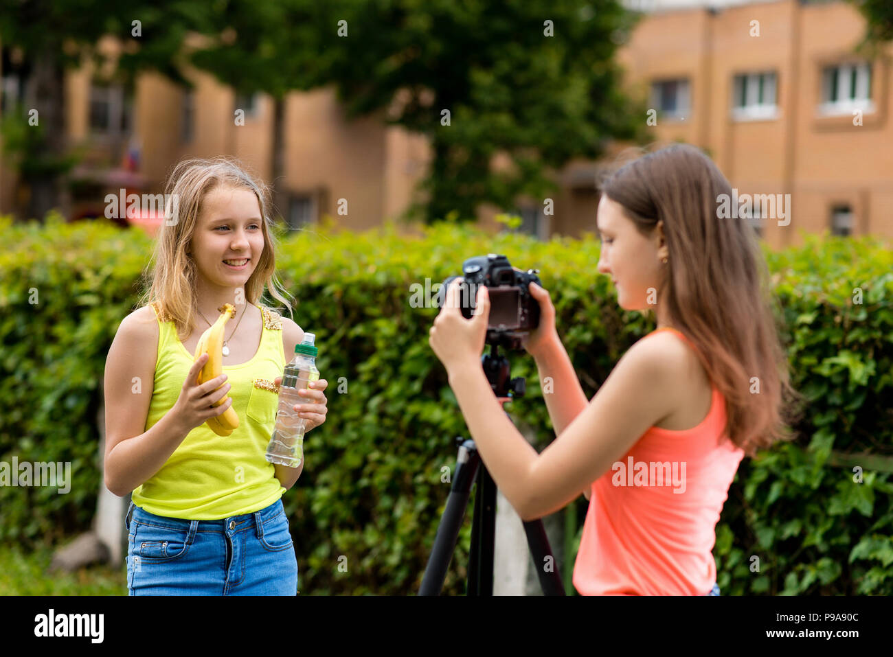Zwei Mädchen Schulmädchen. Im Sommer in der Stadt. Schreibt das Video auf der Kamera. In den Händen hält, Bananen und eine Flasche Wasser. Das Konzept einer Video Blog über gesunde Ernährung. Stockfoto