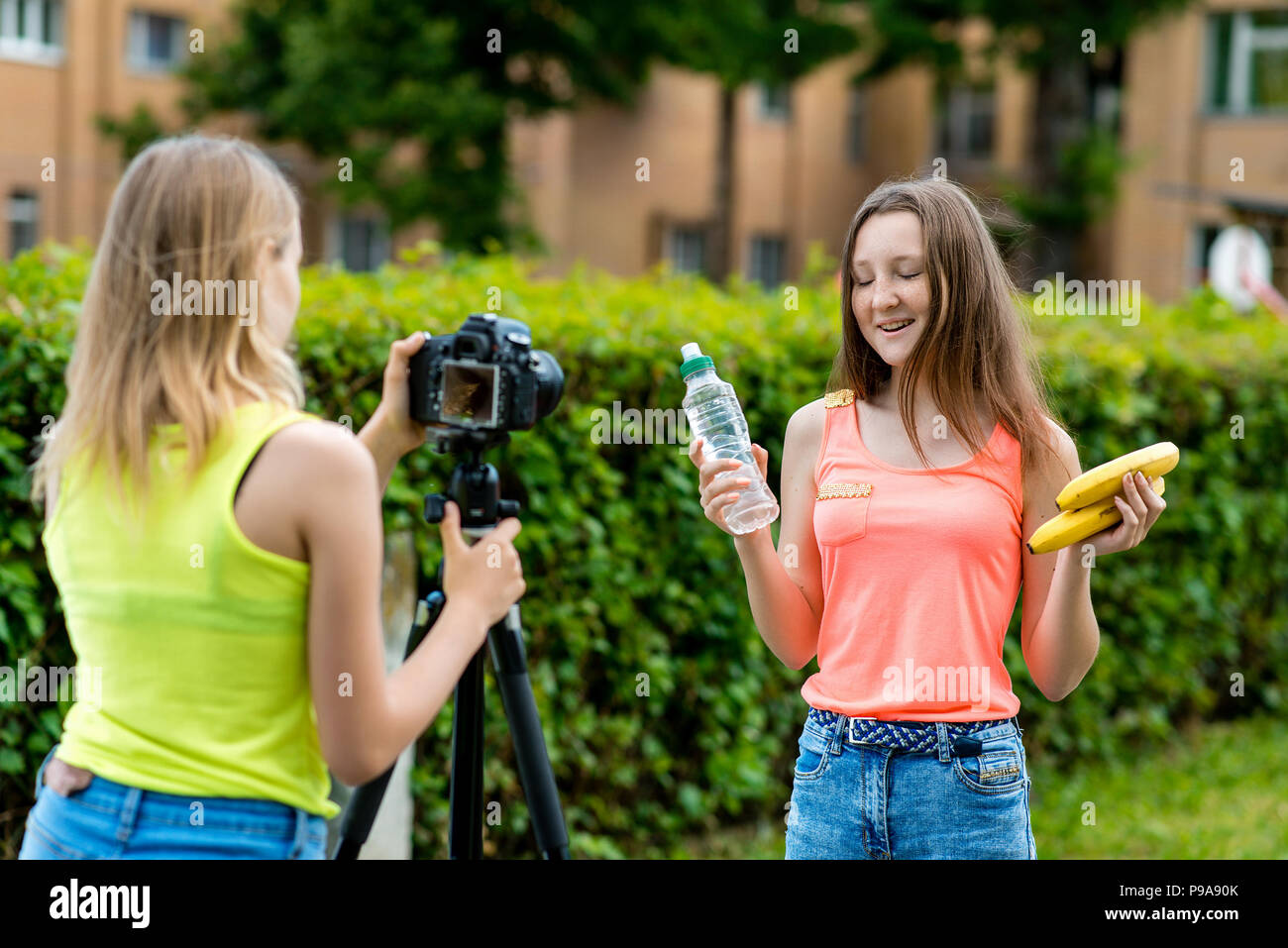 Für Mädchen Schoolgirls, Sommer in der Natur. Records ein Video über das gesunde Essen. In den Händen halten sie eine Banane Flasche mit Wasser. Verwenden Sie die Kamera mit einem Stativ. Stockfoto