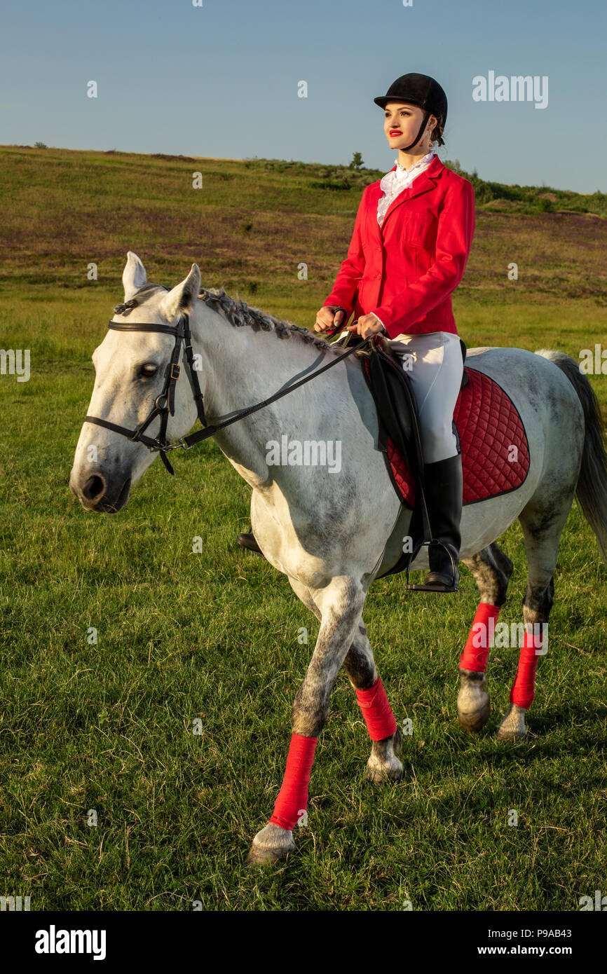 Junge Frau Reiter, das Tragen der roten redingote und weißen Hosen, mit ihrem Pferd in den Sonnenuntergang am Abend Licht. Stockfoto