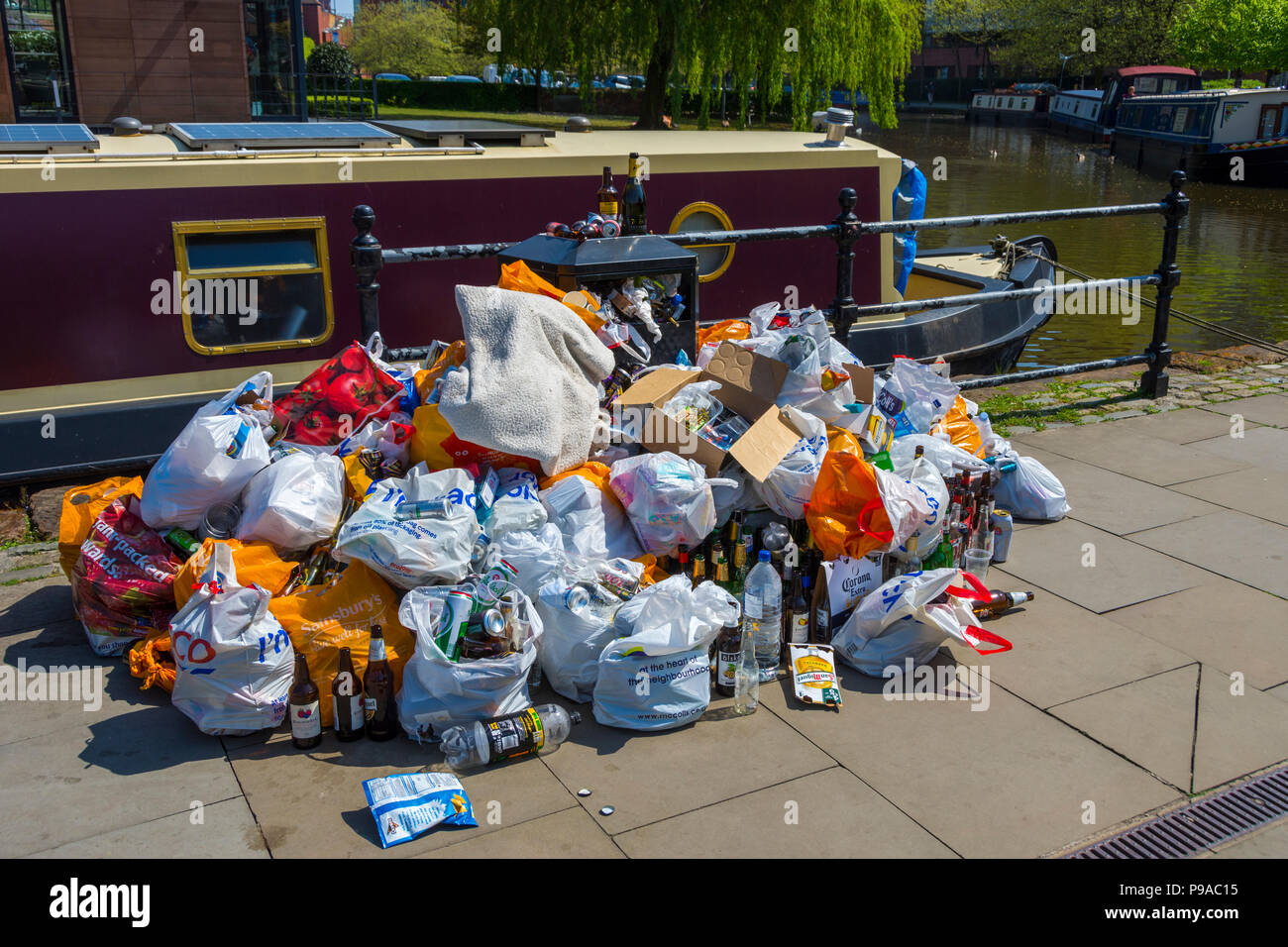 Säcke mit Müll um einen überquellenden Mülleimer nach einem heißen und sonnigen Bank Holiday Wochenende, Castlefield Becken, Manchester, England, Großbritannien Stockfoto