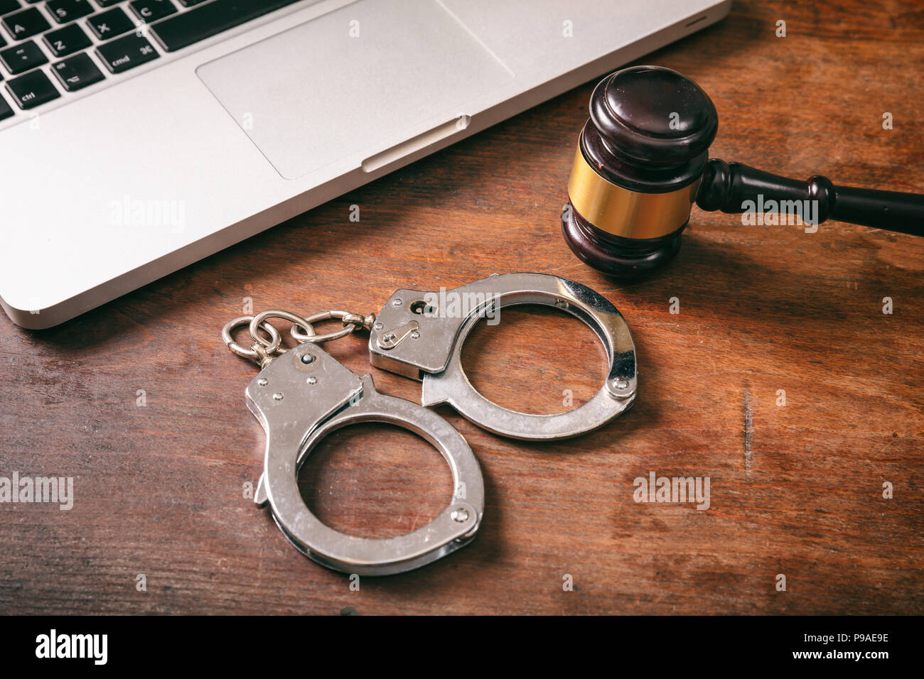 Cyberkriminalität und das Gesetz Konzept. Handschellen und ein Richter Hammer und ein Computer in einem Holz- Hintergrund. Stockfoto