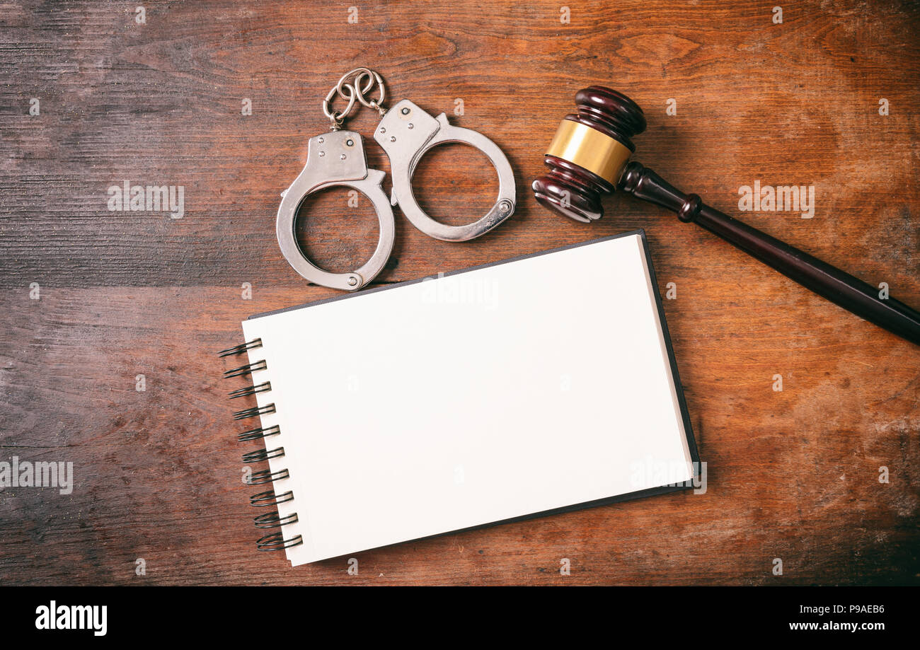 Recht und Ordnung Konzept. Handschellen, Hammer und ein Notebook auf einem hölzernen Hintergrund mit kopieren. Stockfoto