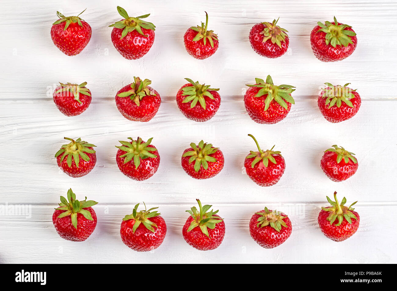 Anordnung der Bio Erdbeeren auf weißem Hintergrund. Reihen von Reife saftige Beeren auf weißem Holz- Oberfläche. Sommer fruchtige Hintergrund. Stockfoto