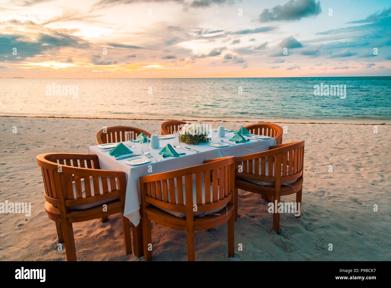 Erstaunliche Familie Tisch Set-up an einem tropischen Strand im Sonnenuntergang. Beruhigende Szene für Abendessen am Strand Stockfoto
