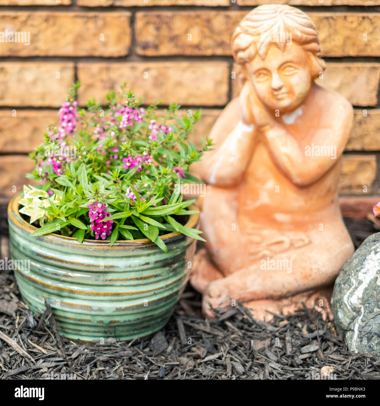 Ein Stein garten Cherub neben einem Topf mit rosa Blumen Angelonia durch eine Mauer aus Stein. USA Stockfoto