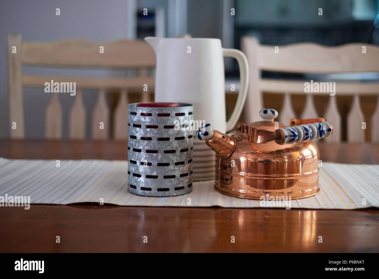 Eine dekorative Gruppierung der einen Krug, ein Kupfer Wasserkocher und ein Zink metall Kerzenhalter auf einem Esstisch mit Runner. USA. Stockfoto