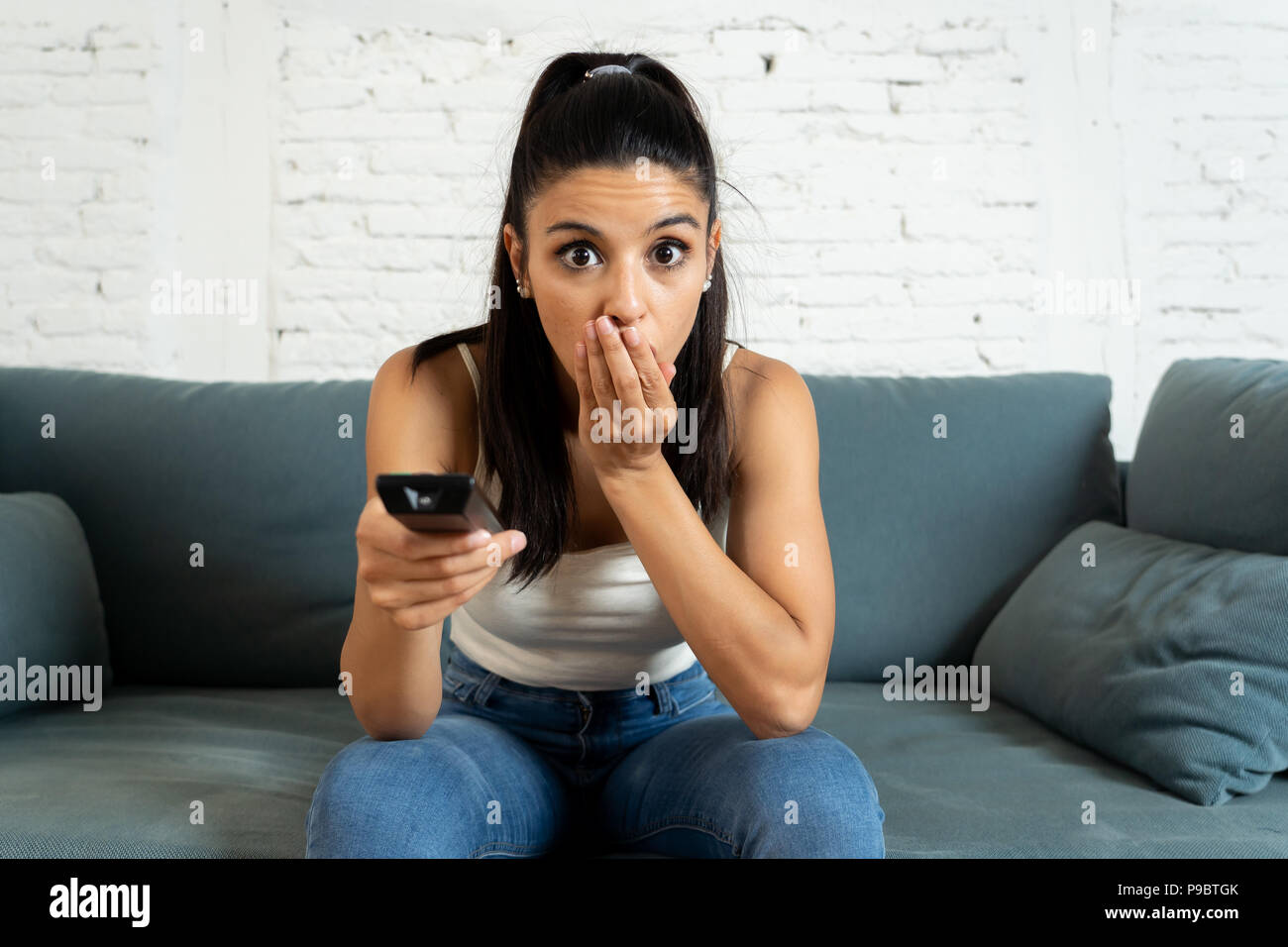 Junge schöne Latin Frau zu Hause Sofa sitzen im Wohnzimmer fernsehen scary Horror Film oder schreckliche Nachrichten ängstlich und aufgeregt, Abdeckung Stockfoto