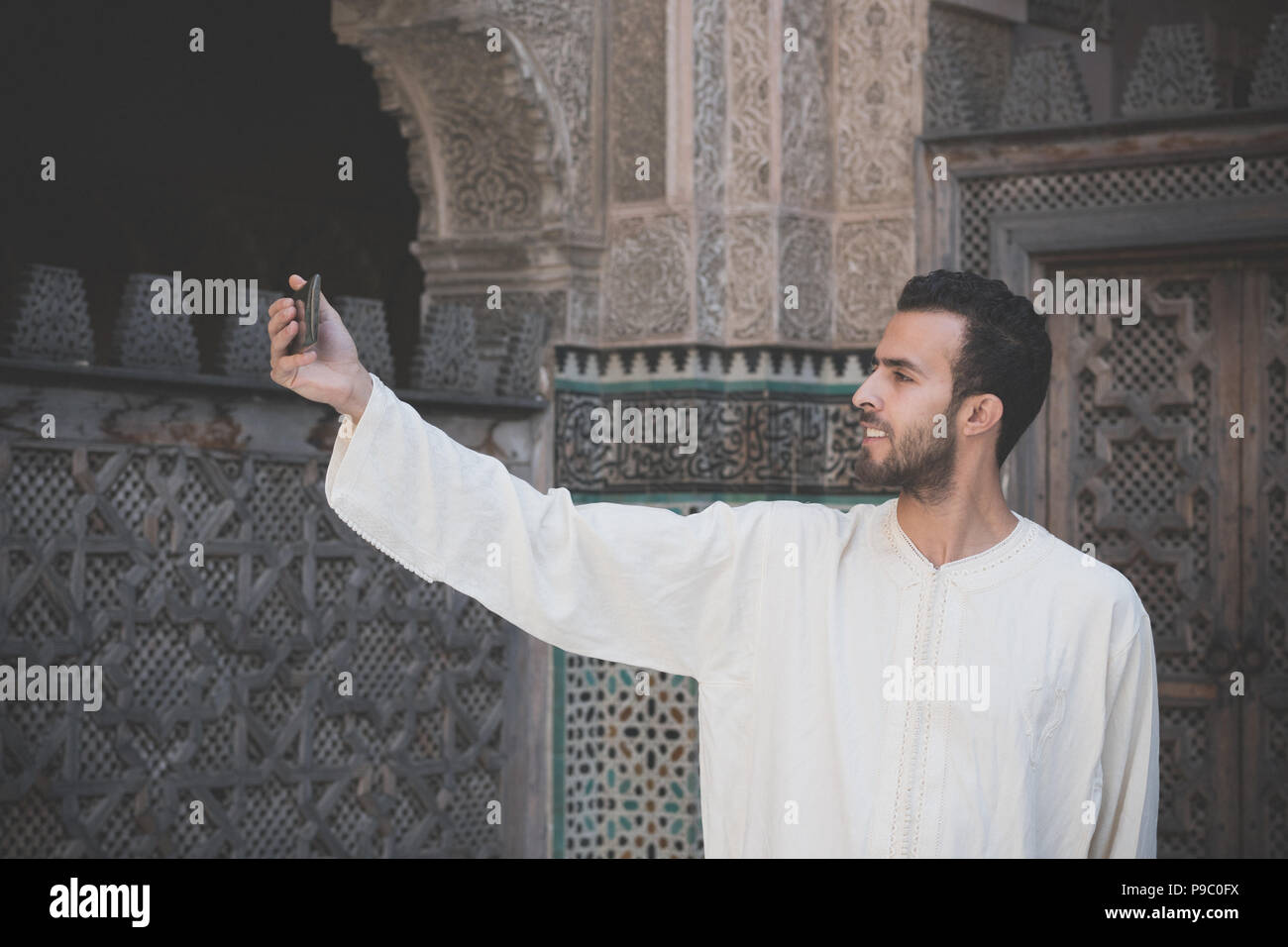 Jahrgang suche Bild von jungen muslimischen Mann in traditioneller Kleidung lächelnd und unter selfie mit Handy Stockfoto