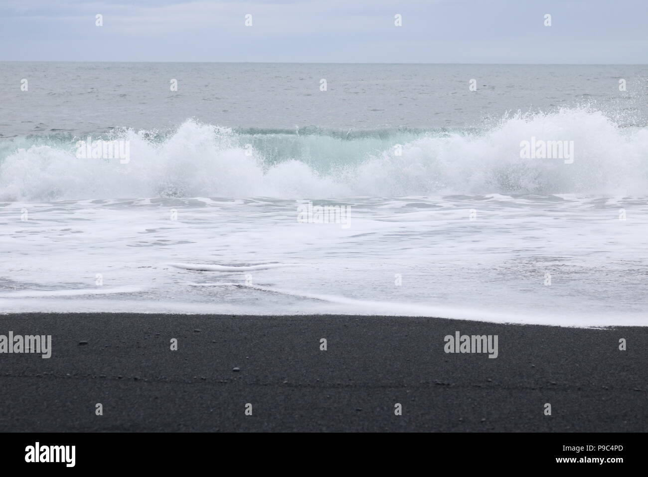 Brechende Welle auf schwarzen vulkanischen Sand Strand in Island Stockfoto