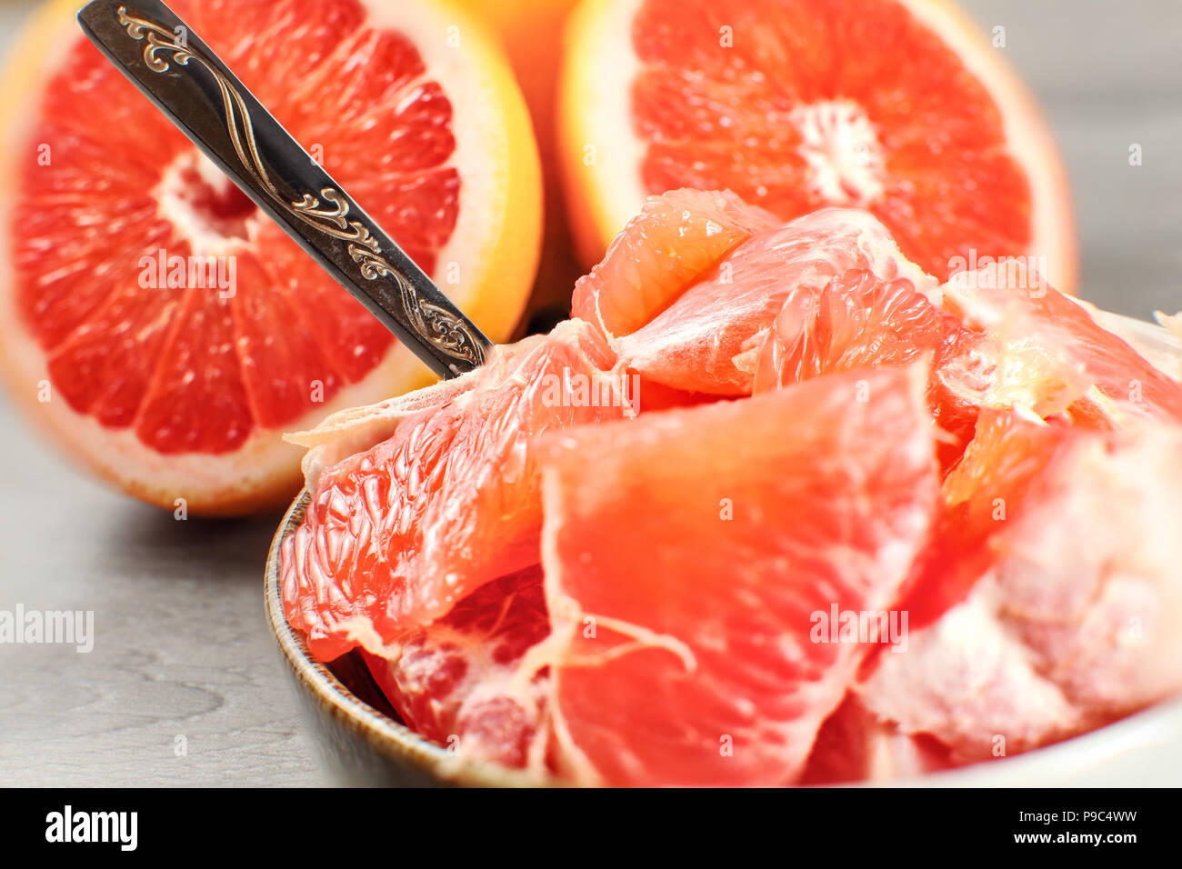 Detail Foto - geschälte Grapefruit in Stücke in kleine Schüssel mit Löffel ausschneiden, mit ganzen Zitrusfrüchte im Hintergrund. Stockfoto