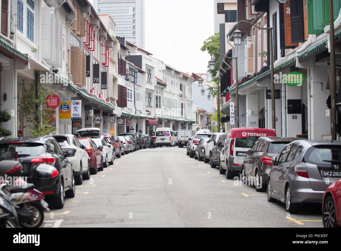 Die Einbahnstraße ist mit Fahrzeugen gefüllt, die an den Seiten vor dem historischen Ladengeschäft geparkt sind. Singapur. Stockfoto