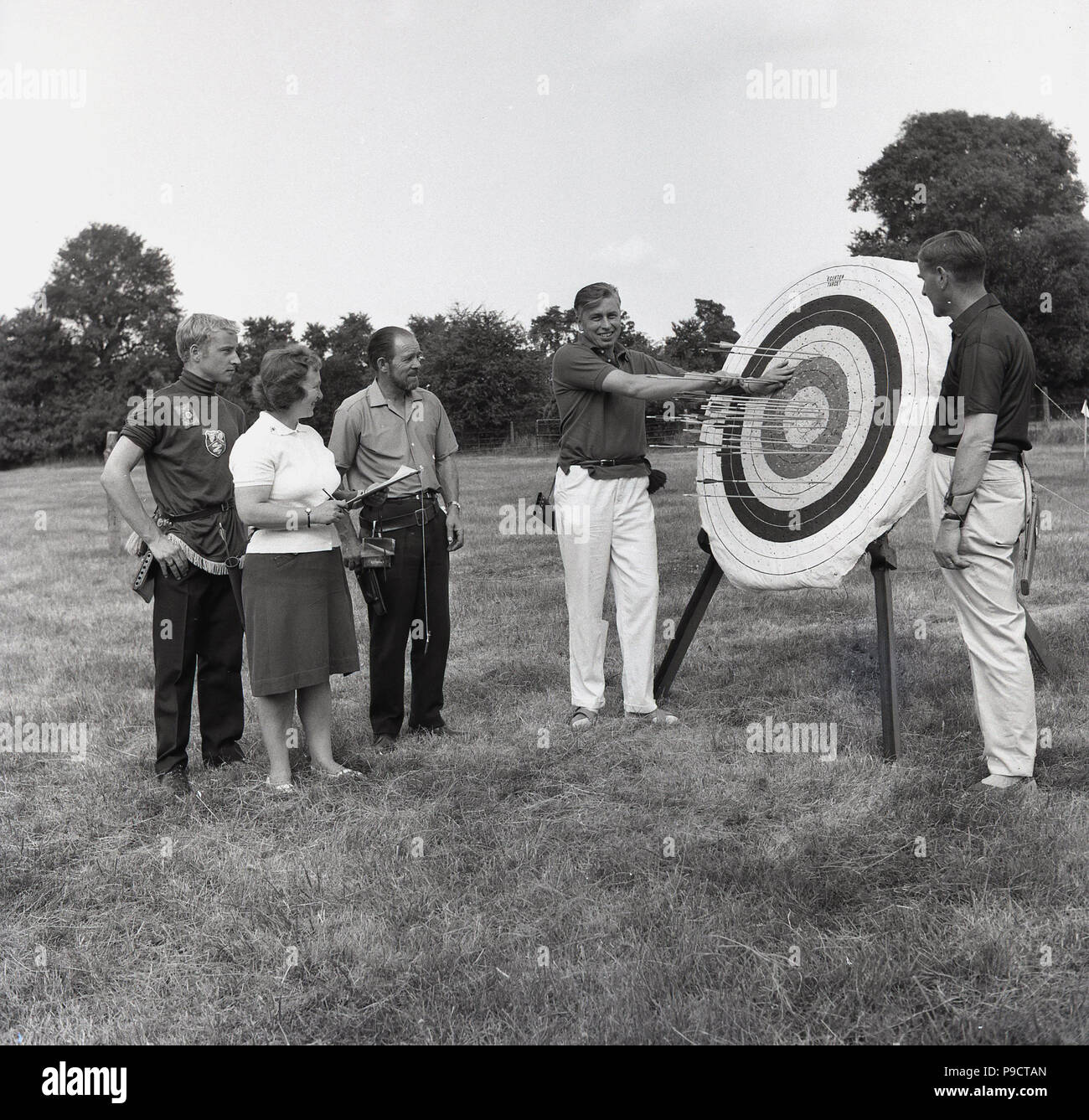 1960, historische, bei einem Dorffest eine Bogenschießen Wettbewerb, Menschen in einem Bereich, der von einem Impulsstück mit Pfeilen im Stehen. Stockfoto