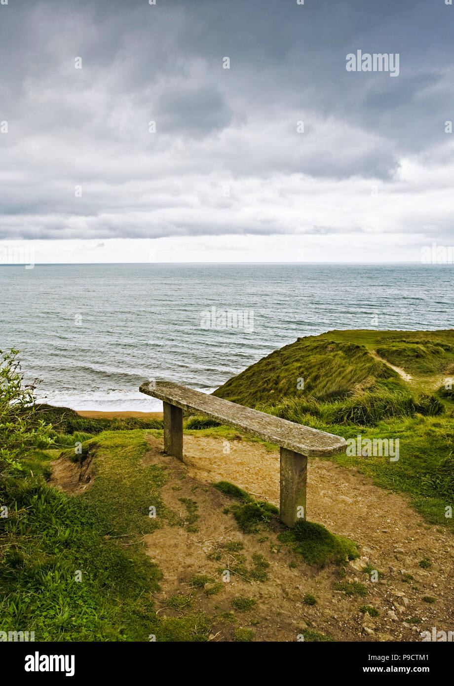Alte Holzbank mit Blick auf das Meer von einer Klippe auf einem grauen bewölkten Tag, England, Großbritannien Stockfoto