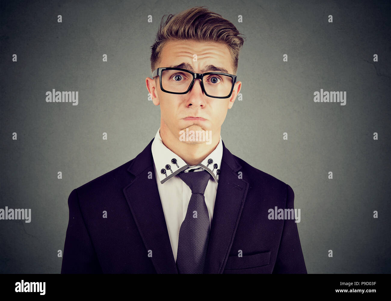 Junge formale Mann in Anzug und Brille suchen beleidigt und Mitleid finsteres Gesicht und schrie auf grauem Hintergrund Stockfoto