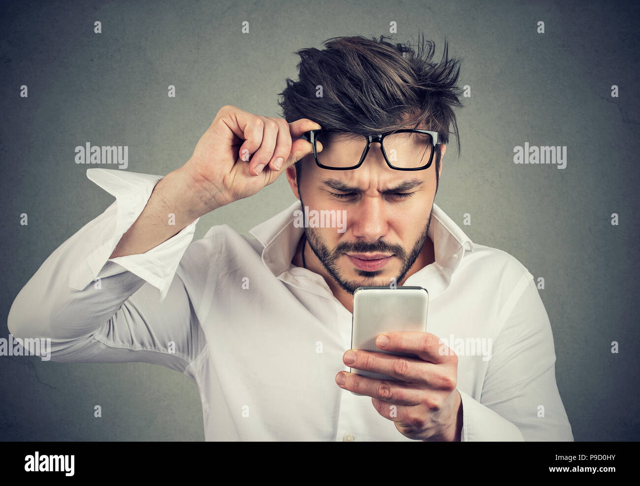 Junge formale Mann lesen Smartphone und Probleme mit den Augen blinzeln auf grauem Hintergrund Stockfoto