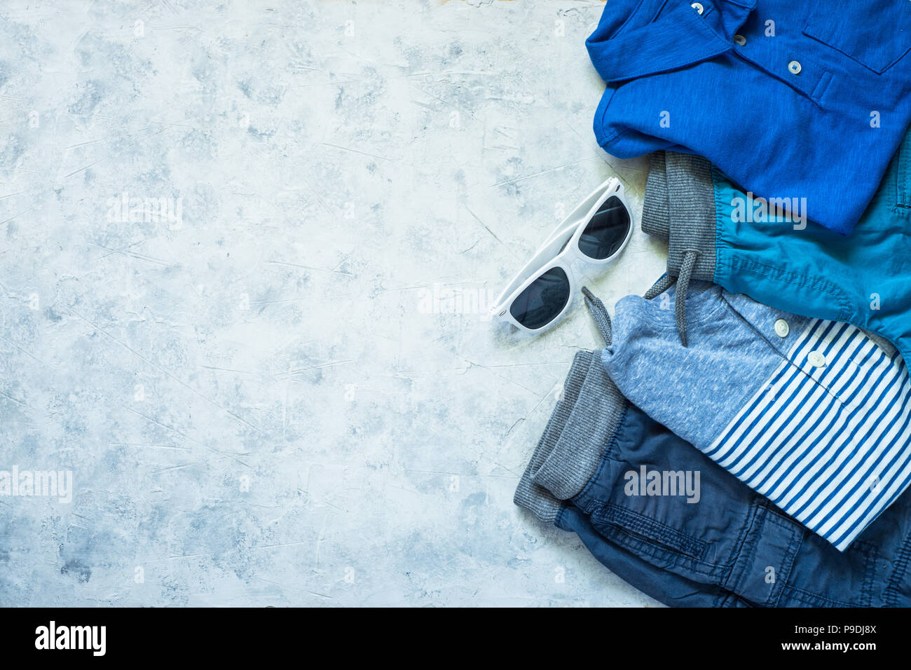 Kind Kleidung - Jeans, Polo, Shorts und Turnschuhen Draufsicht auf Stein Hintergrund. Mode Beauty Hintergrund. Modernes Aussehen. Flach kopieren. Stockfoto