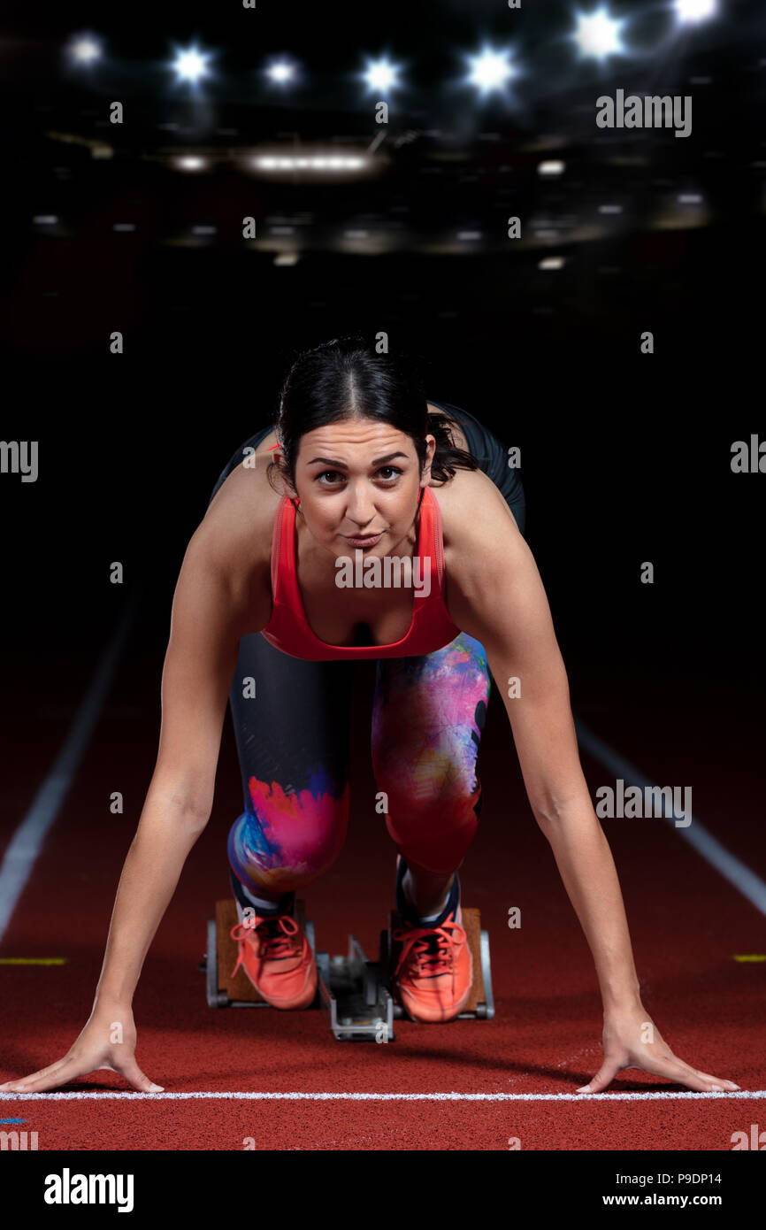 Frau Sprinter verlassen Start auf der Leichtathletikbahn. explodierende Start am Stadion mit Reflektoren Stockfoto